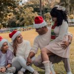 A joyful family wearing Santa hats enjoying Christmas in a sunny park.