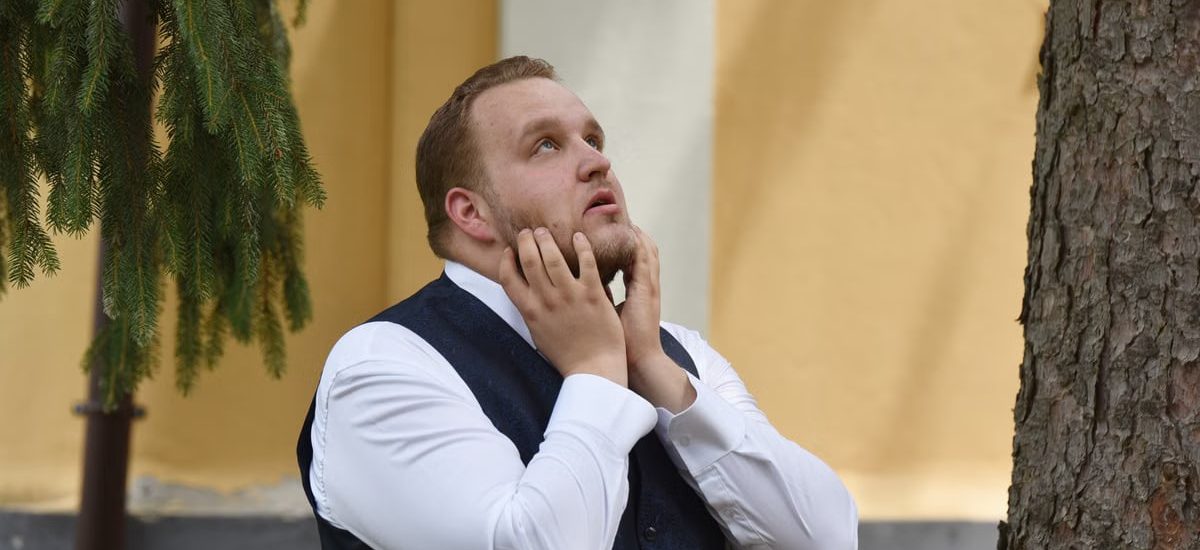 A man in formal attire looks contemplative under trees in Vásárosnamény.