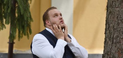 A man in formal attire looks contemplative under trees in Vásárosnamény.
