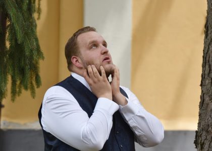 A man in formal attire looks contemplative under trees in Vásárosnamény.